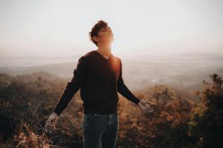 A young man standing on a misty hill during sunrise, embracing the light and nature.