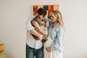 A joyful expecting couple with their Bengal cat, sharing a moment of affection indoors.